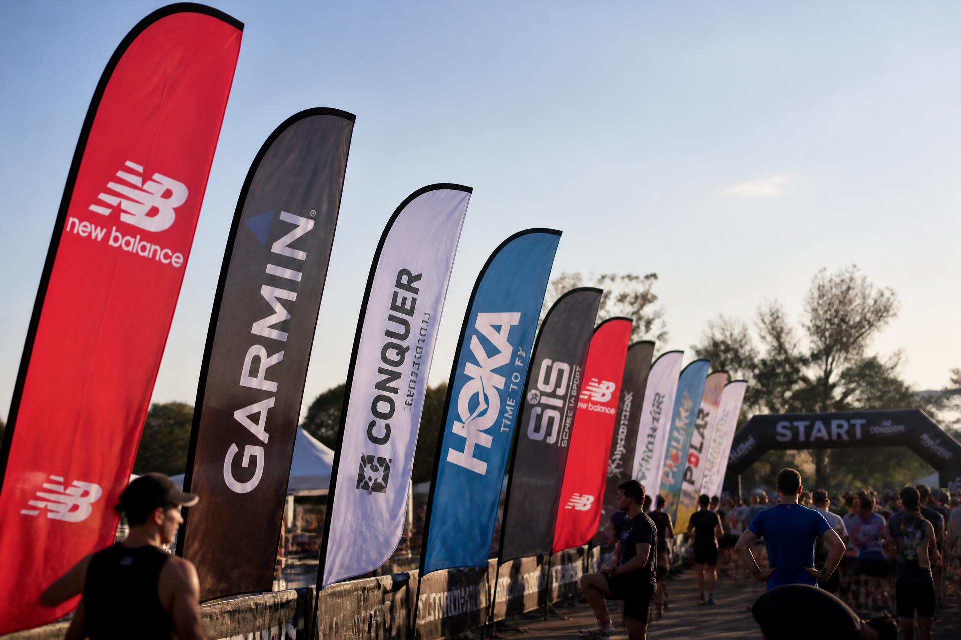 Rij kleurrijke beachflags met sponsorlogo's bij de start van een hardloopevent